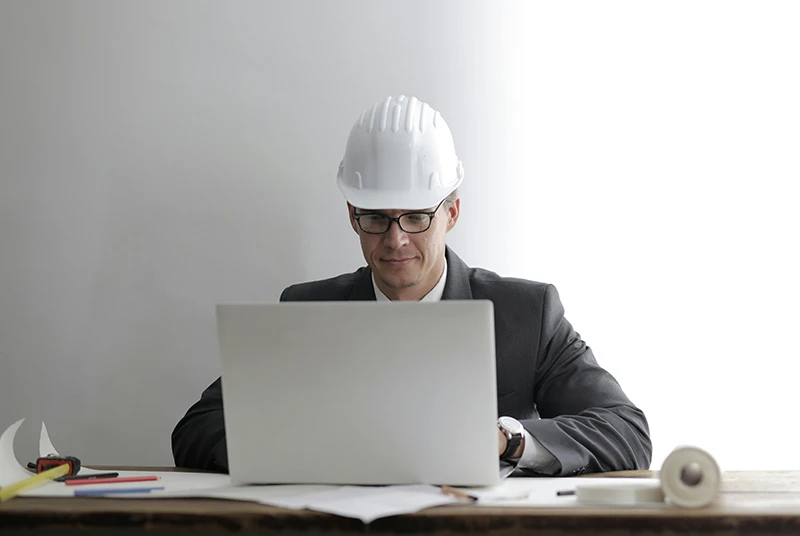 Construction site supervisor wearing a hard hat reviewing plans on a laptop
